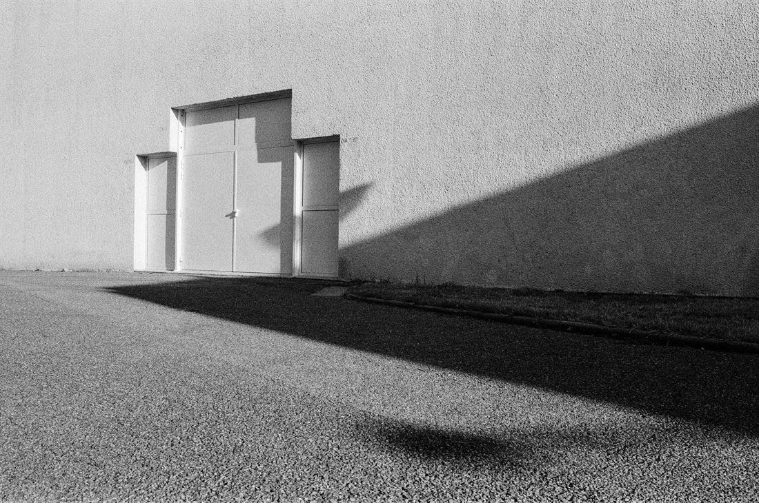 Chabeuil, noir et blanc très graphique, angles, murs blanc vif, grand portail blanc métallique, route goudronnée grise, 